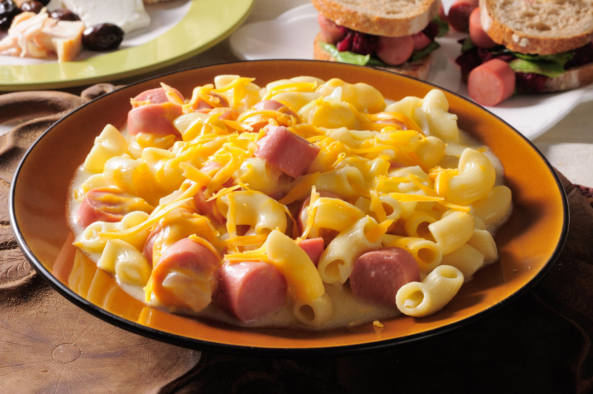 In a casserole, mix macaroni with 2 cups cheese and U.S. chicken franks. Sauté onion in butter in a pan over medium heat until soft. Stir in flour and milk quickly until combined. Season with salt and pepper. Pour mixture over franks and stir well. Sprinkle remaining cheese on top. Cook inside oven for 20 minutes or until heated through.
